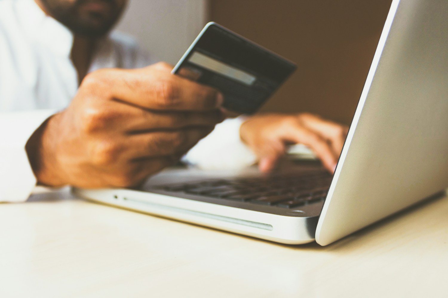 A person holding a payment card while using a laptop